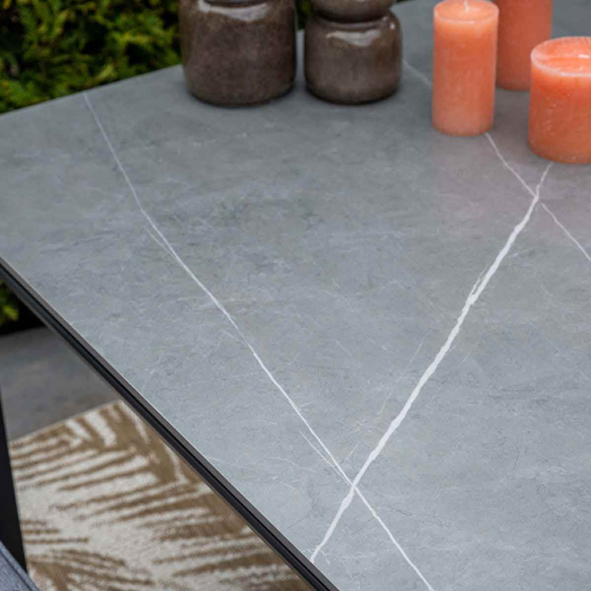Close-up van een grijze tafel met marmerlook met kaarsen en decoratieve items. Groene planten op de achtergrond.