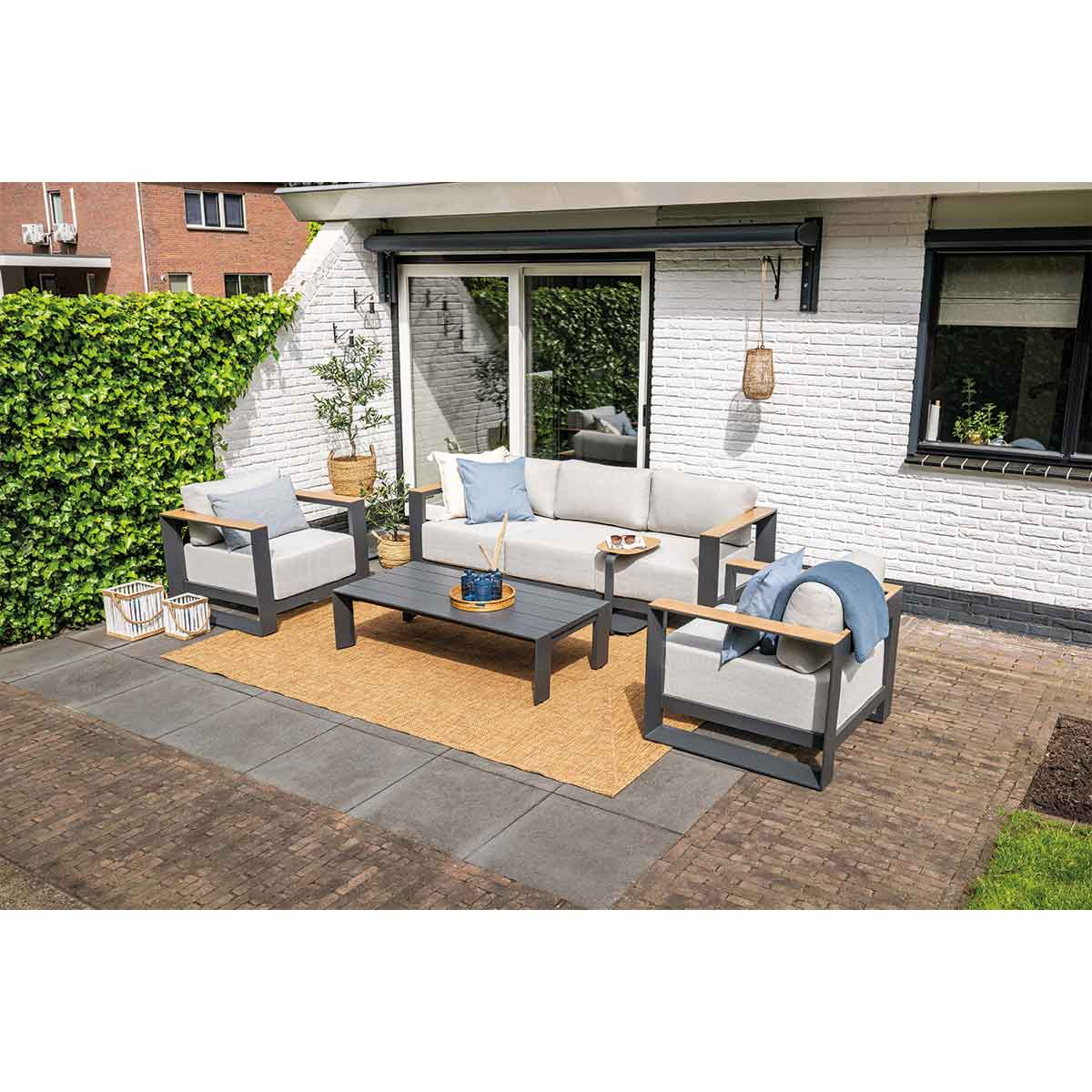 Buitenterrasset: bank, twee stoelen, salontafel. Bakstenen terras, witte muur.