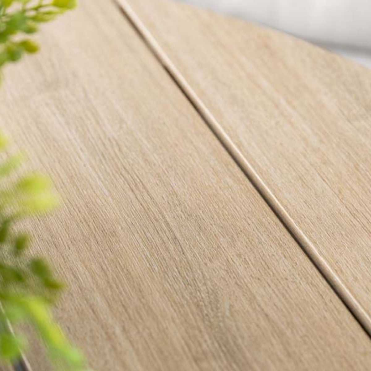 Close-up of a light wood table. The wood grain is visible. A subtle line runs down the middle.