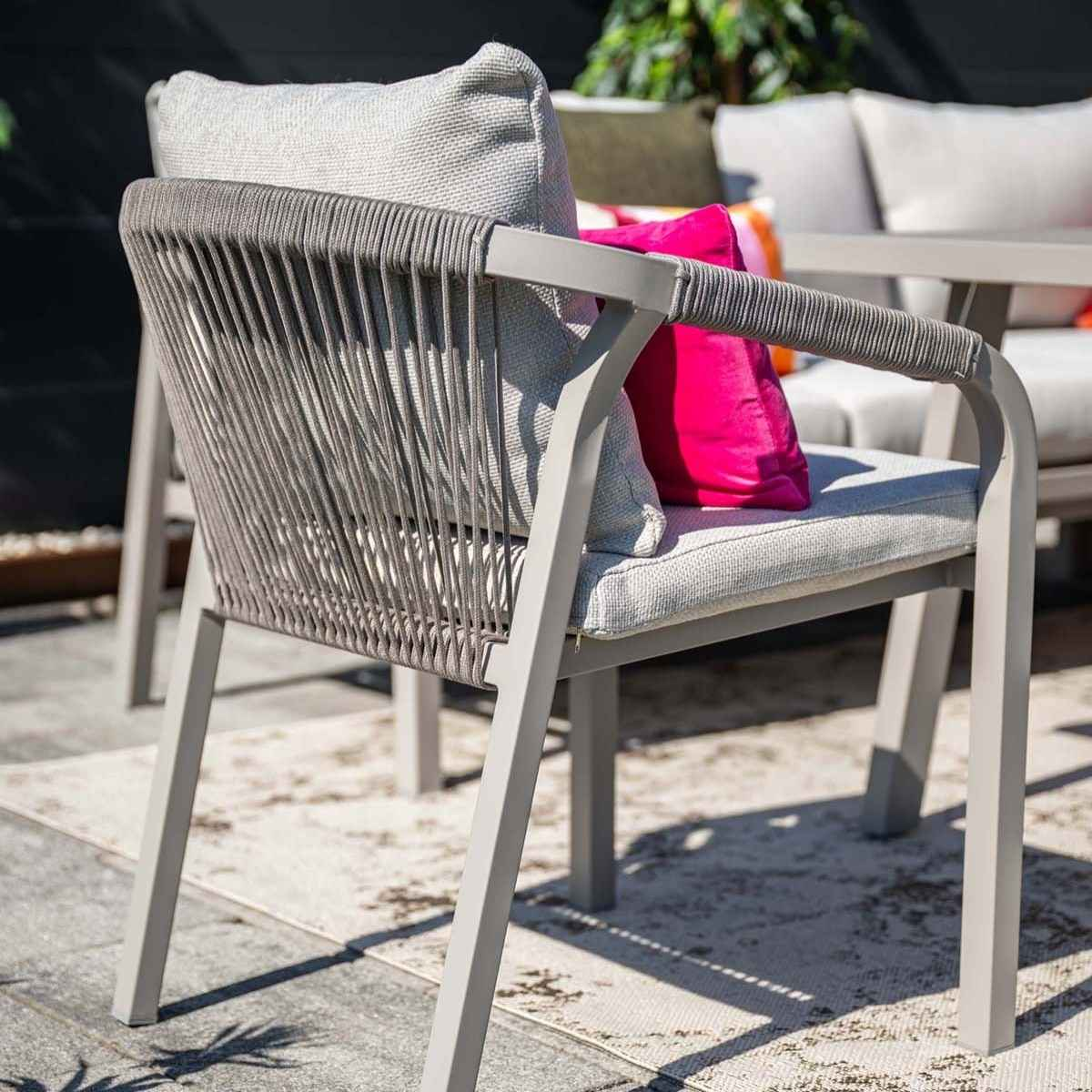 Outdoor chair with grey frame, grey cushion, and pink pillow. Rattan-like back. On a patio.