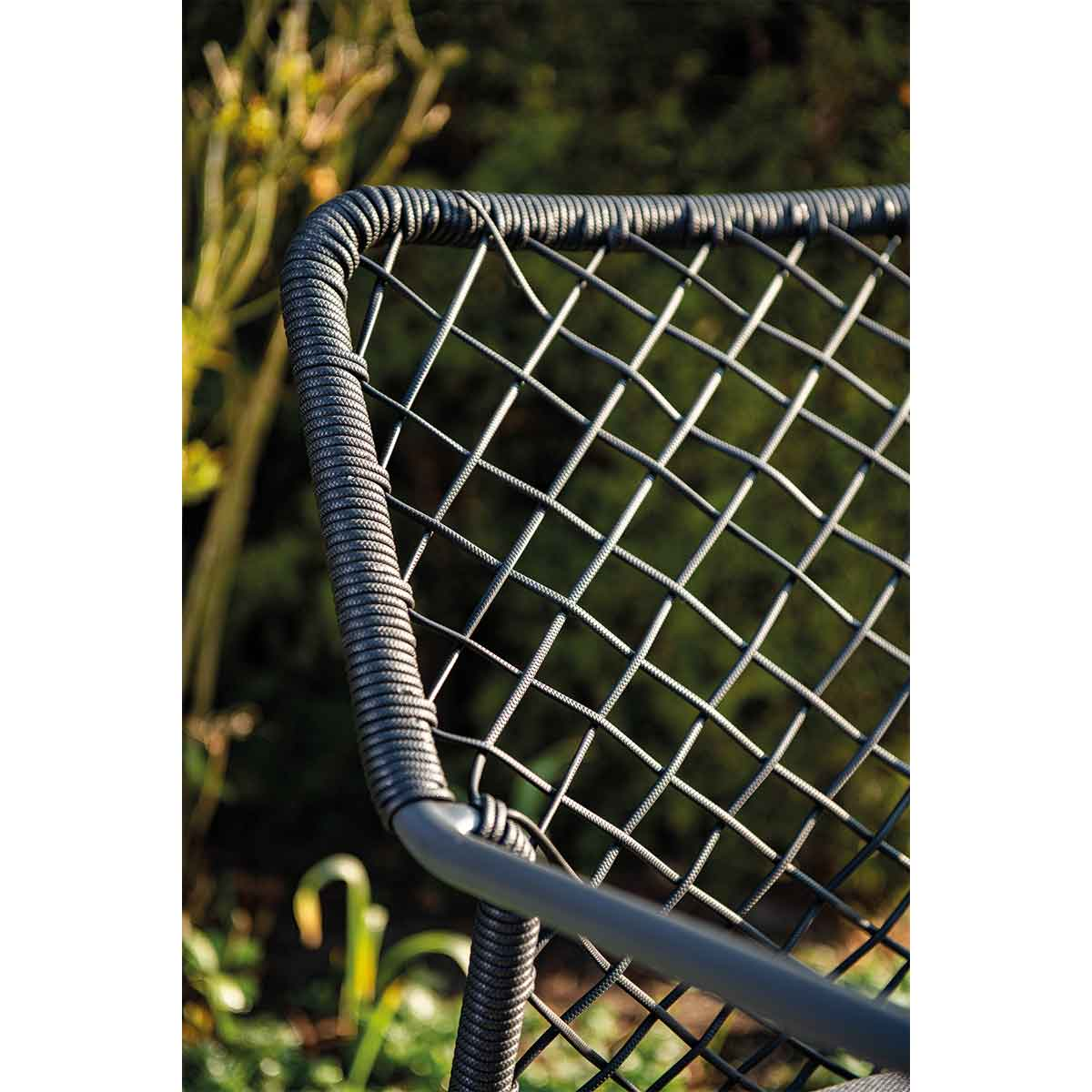 Close-up of chair back. Dark grey rope-like woven detail. Blurred green background.