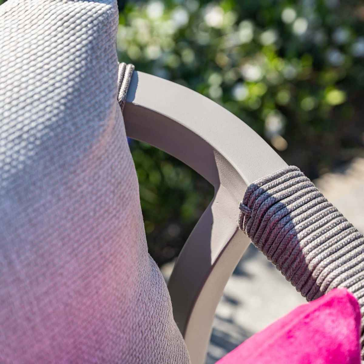 Gros plan sur un accoudoir de chaise avec un coussin rose et des détails de corde grise.