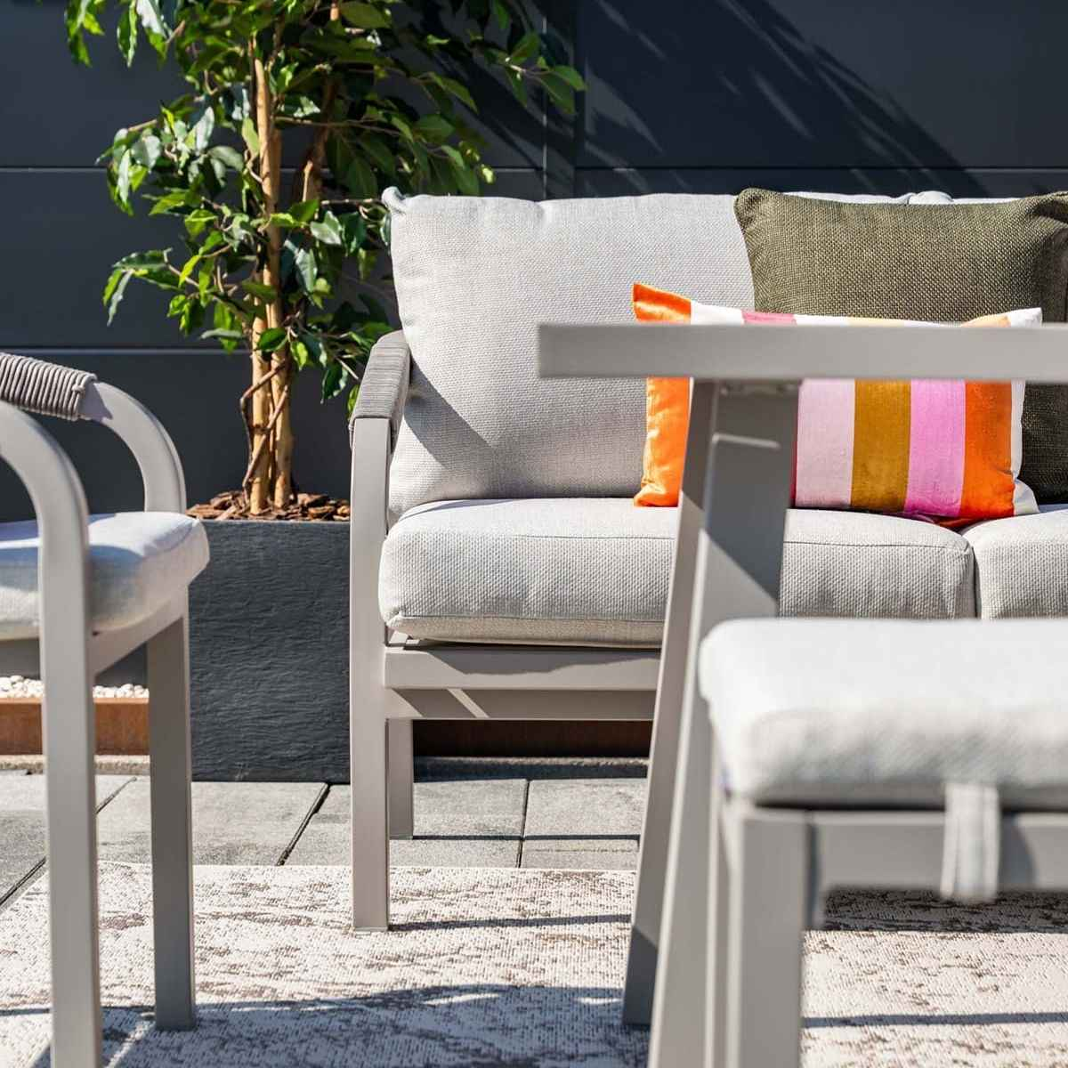 Mobilier d'extérieur. Coussins gris et oreiller rayé coloré. Arbre en pot en arrière-plan.