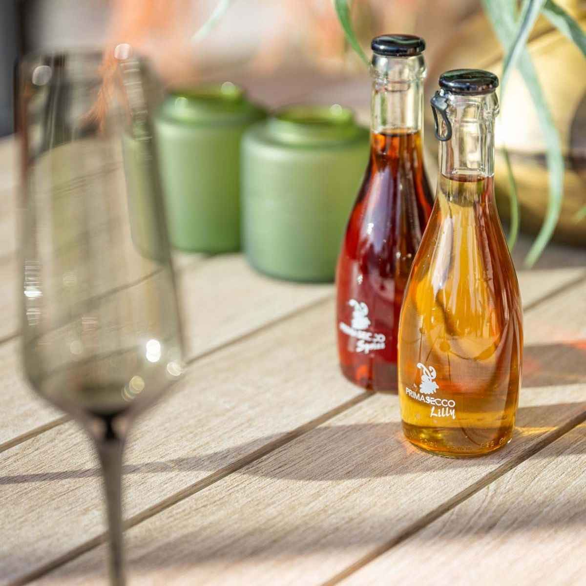 Close-up of bottles with liquids and a wine glass on a wooden table.