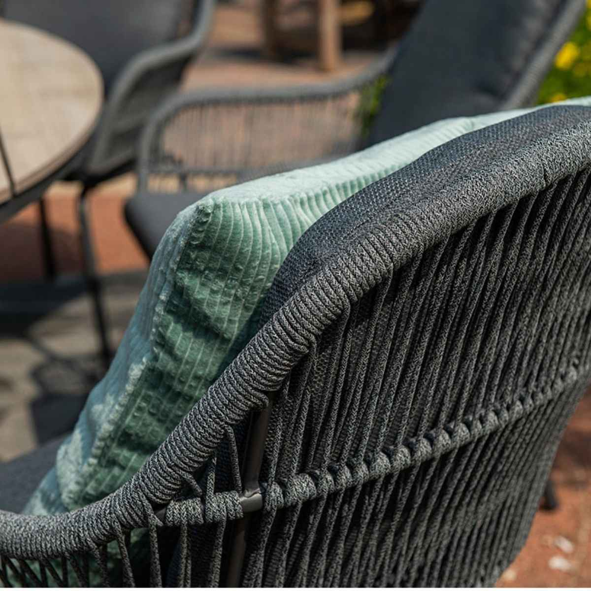 Close-up of chair: grey woven back and cushion, mint green pillow.