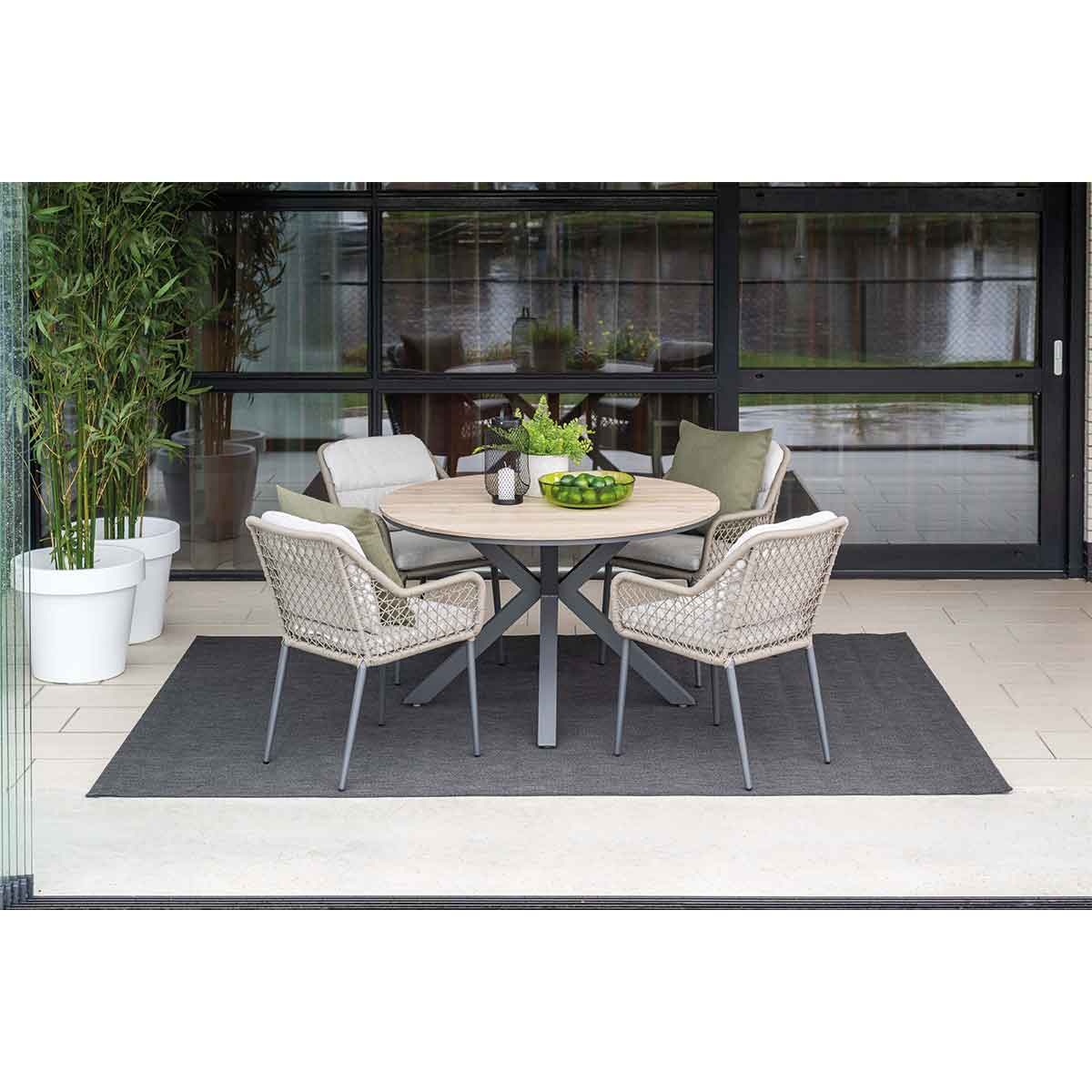 Ensemble repas extérieur avec une table ronde et quatre chaises. Chaises beiges, table en bois clair.