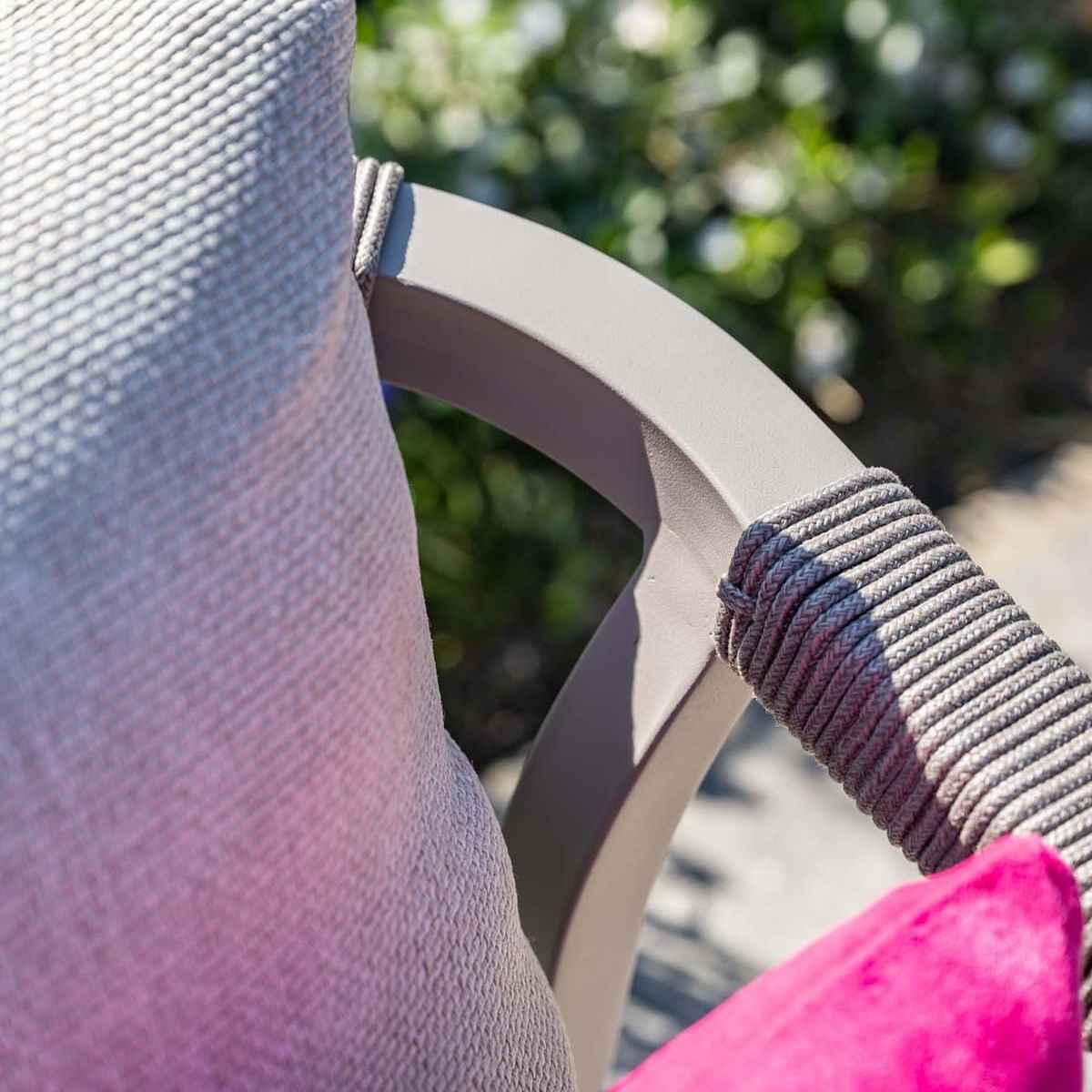 Gros plan sur le bras de la chaise, cadre gris, avec coussin rose. Focus sur le détail de la corde tissée.