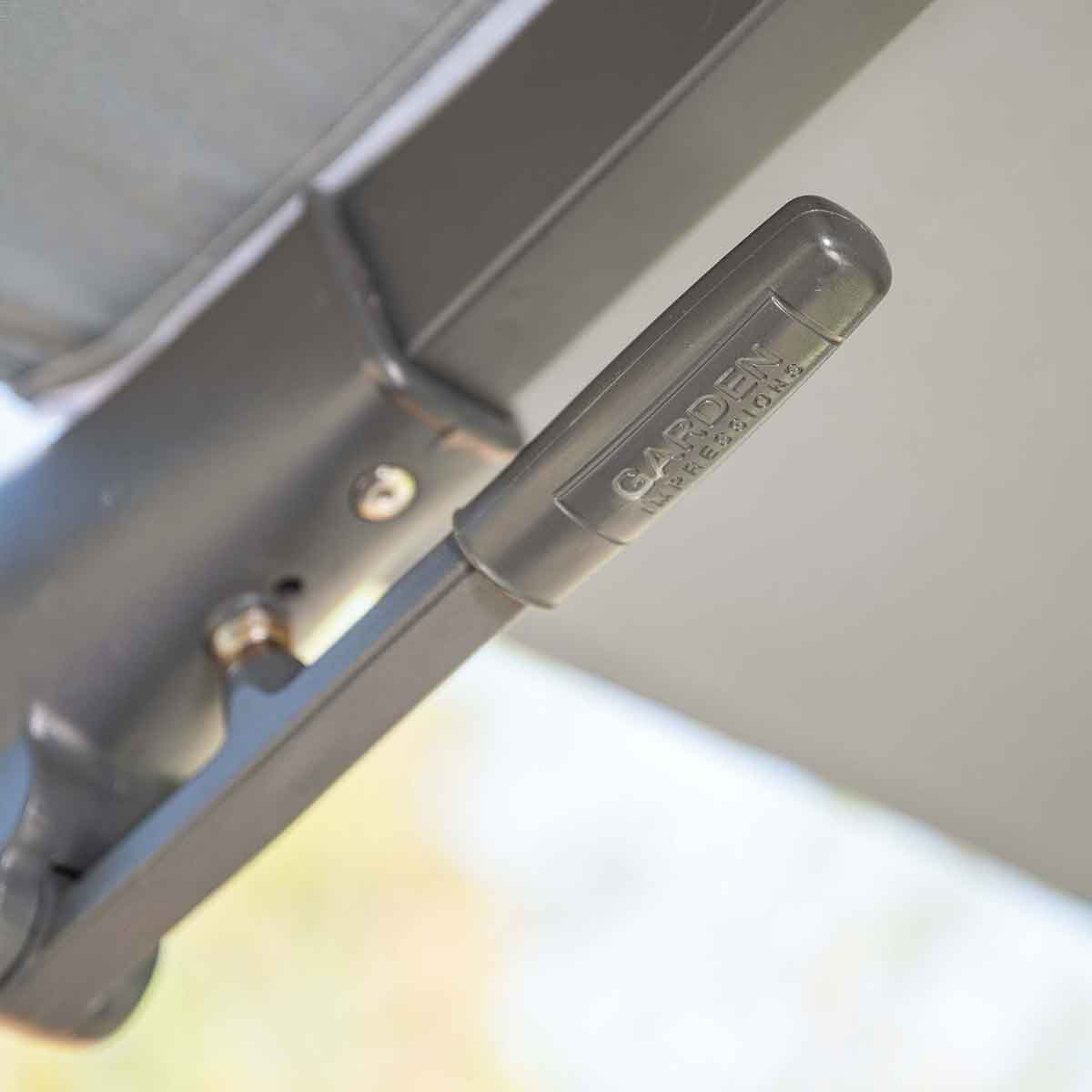 Close-up van een grijs parasolmechanisme met het label 'GARDEN IMPRESSIONS'.