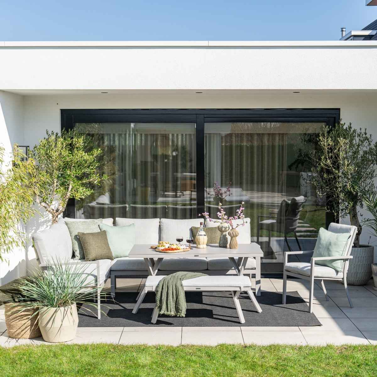 Ensemble de patio extérieur. Canapé, table, banc et chaises gris. Herbe verte et plantes autour.