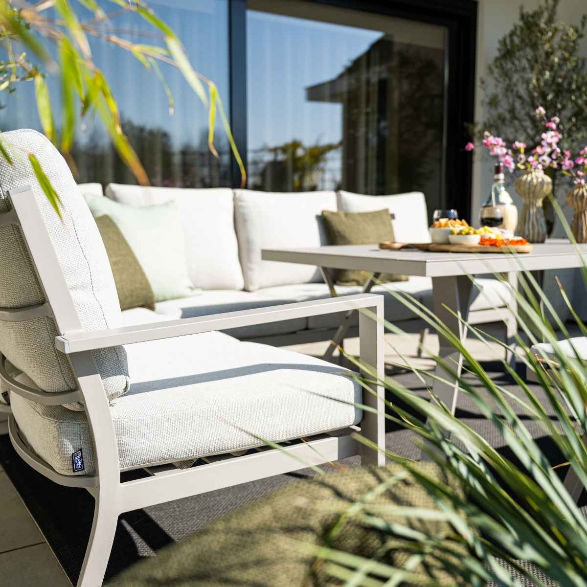 Coin salon extérieur avec canapé et chaise. Coussins beiges, cadre foncé, table avec collations.