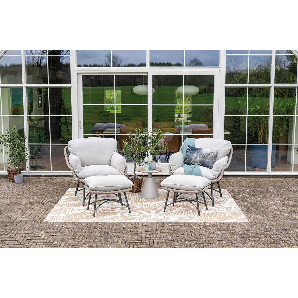 Outdoor seating area with two chairs and an ottoman on a patterned rug near a glass wall.
