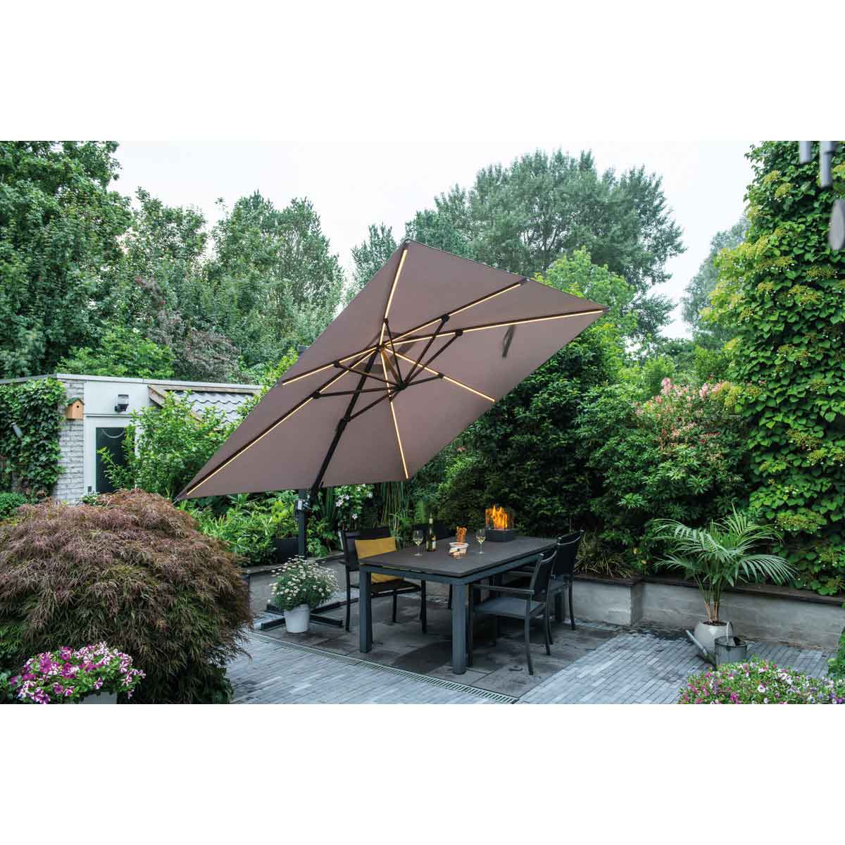 Scène de patio avec un grand parasol incliné au-dessus d'une table et des chaises, entouré de verdure.