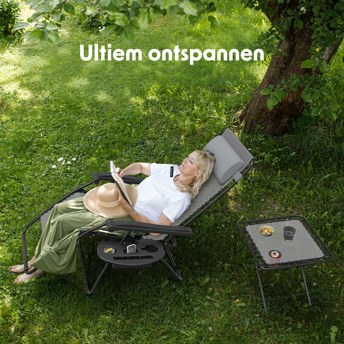 Een vrouw ontspant in een grijze ligstoel met een bijzettafel en geniet van de buitenlucht.