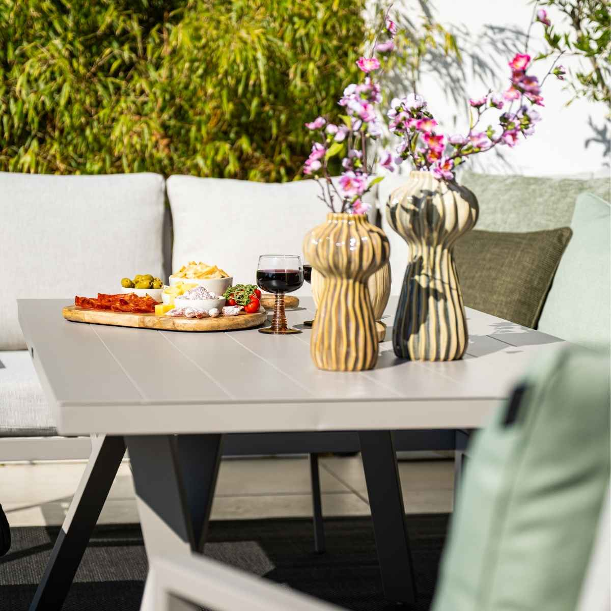 Table avec nourriture et fleurs, dressée pour dîner sur un patio avec des sièges.