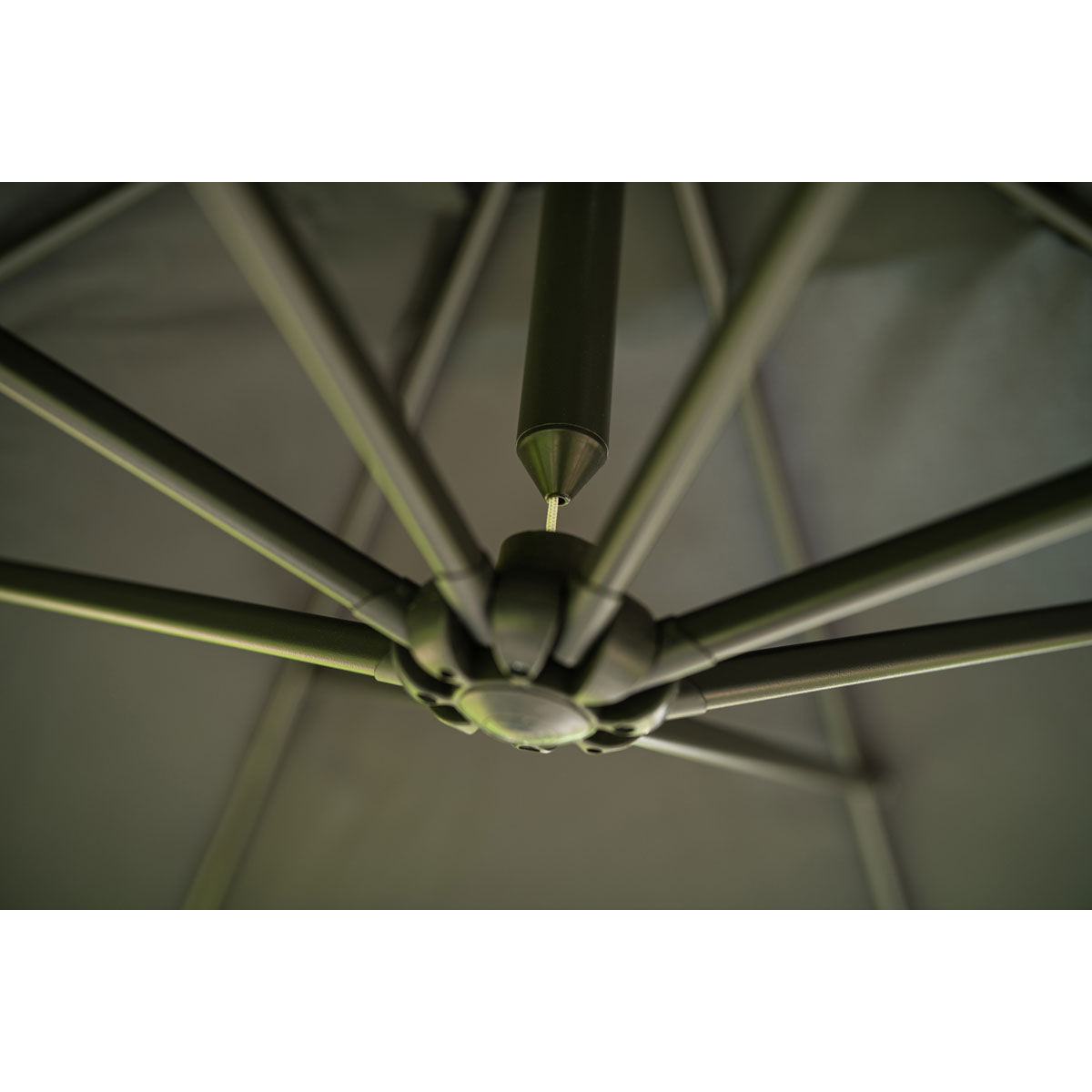 Close-up of an umbrella's central hub with radial supports. Grey fabric and dark metal frame.