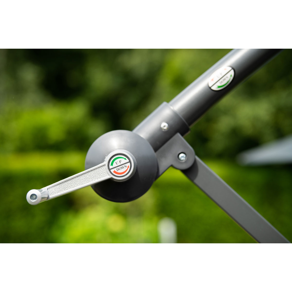 Gros plan sur la poignée d'un parasol cantilever gris, fond vert.