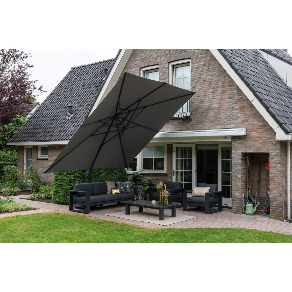 A gray cantilever umbrella is over a patio set. A brick house is in the background.