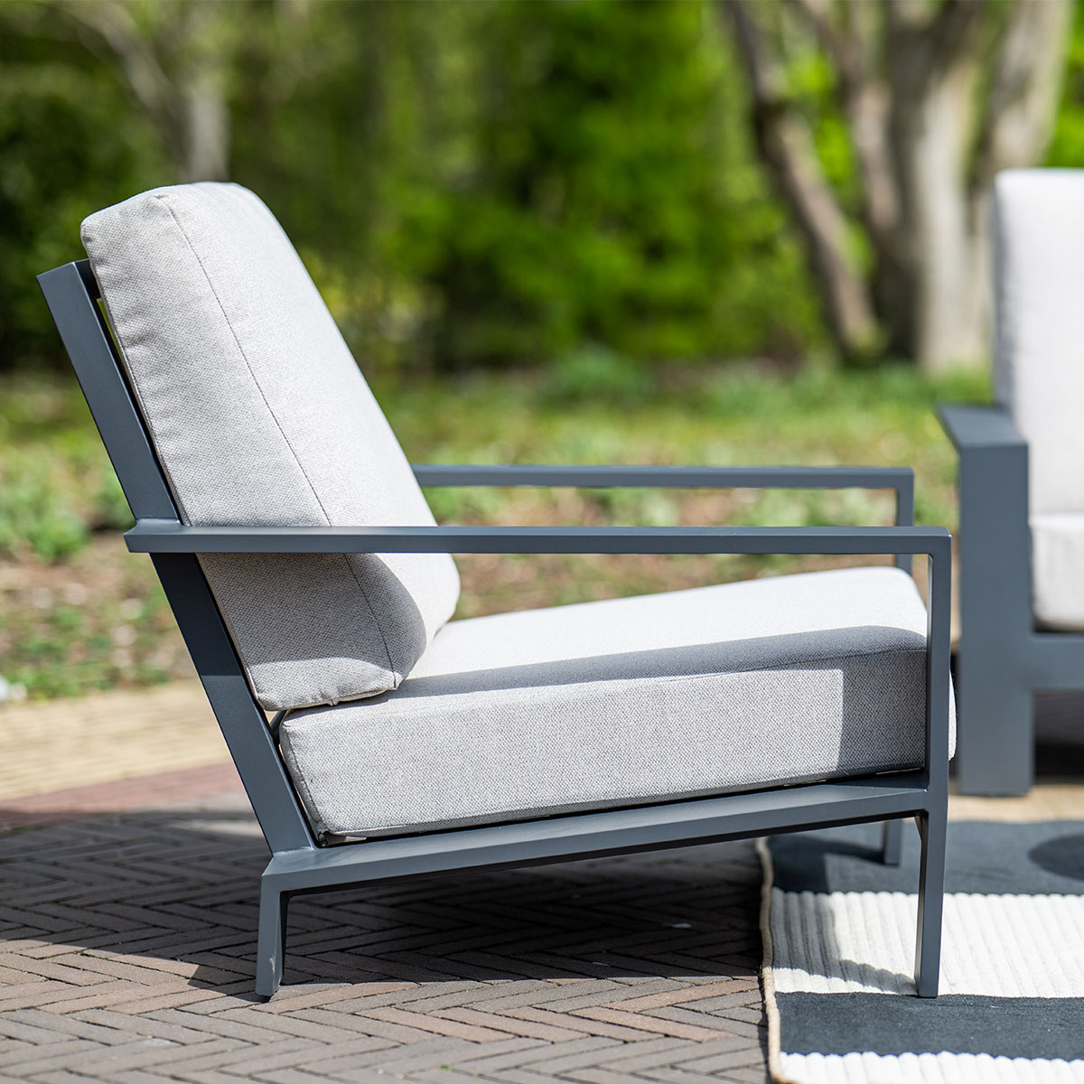 Grey outdoor chair with a frame and cushion, brick patio background.