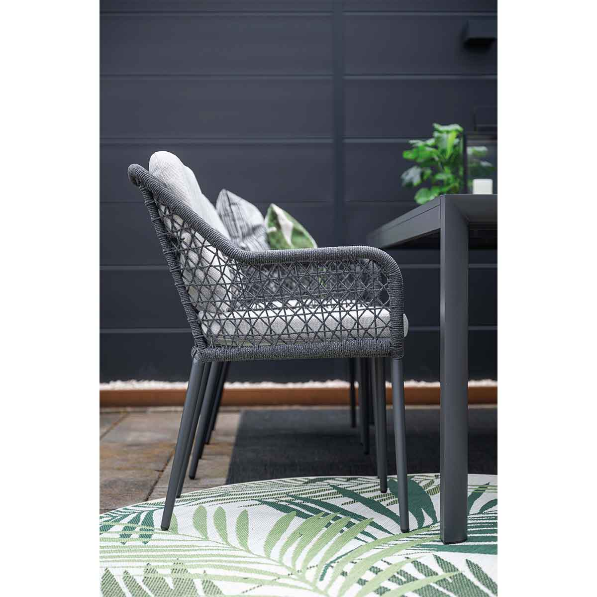 Outdoor seating area with grey chairs, a table, and a leafy rug.