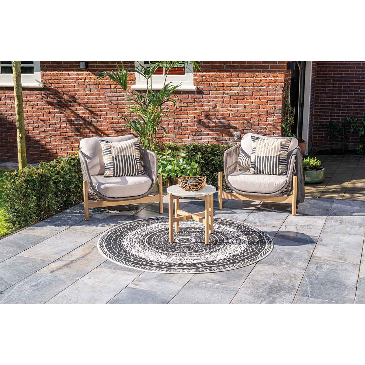 Outdoor seating area with two chairs, small table, and a rug on tiled patio.