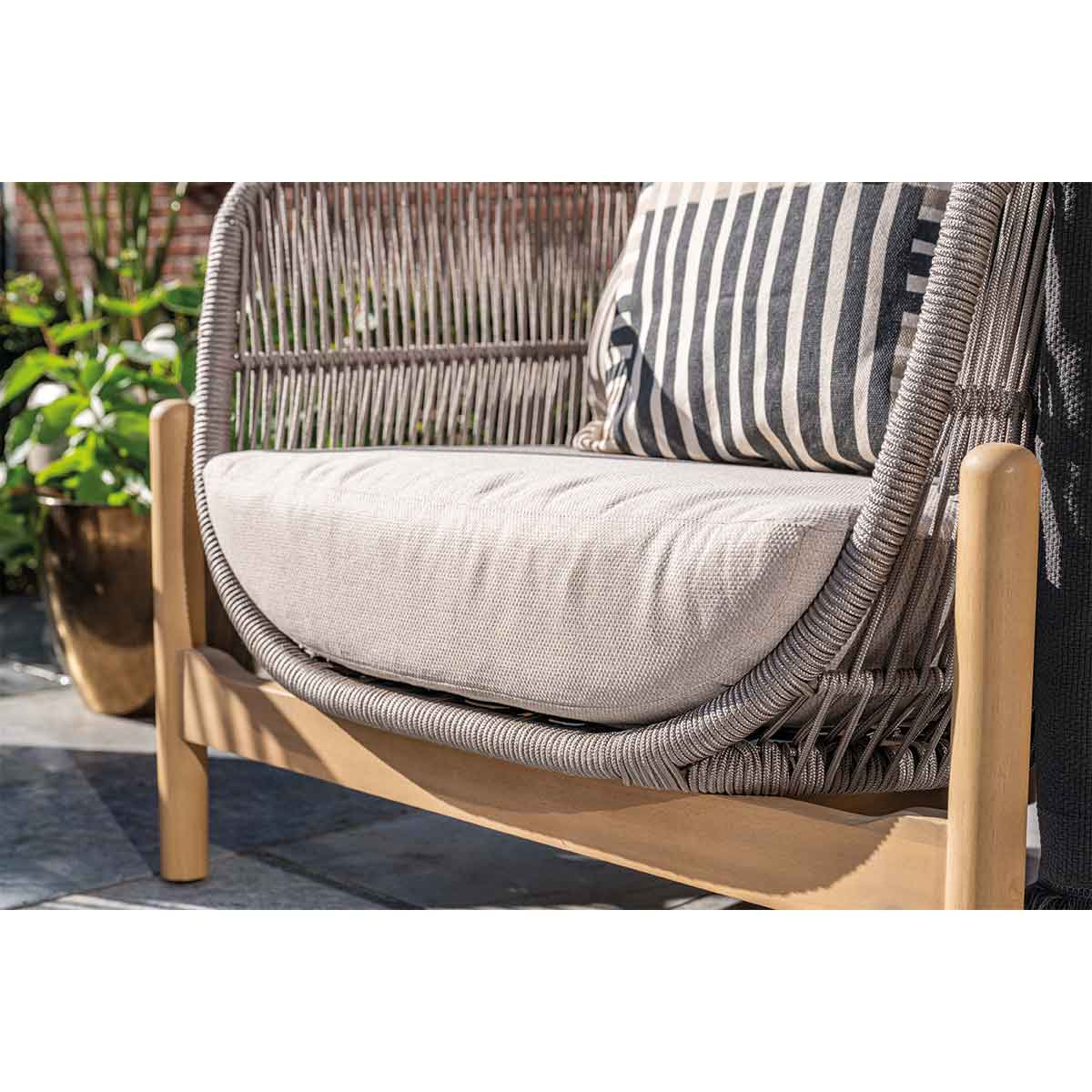 Close-up of an outdoor chair with a wooden frame, woven back and seat, and a striped cushion.