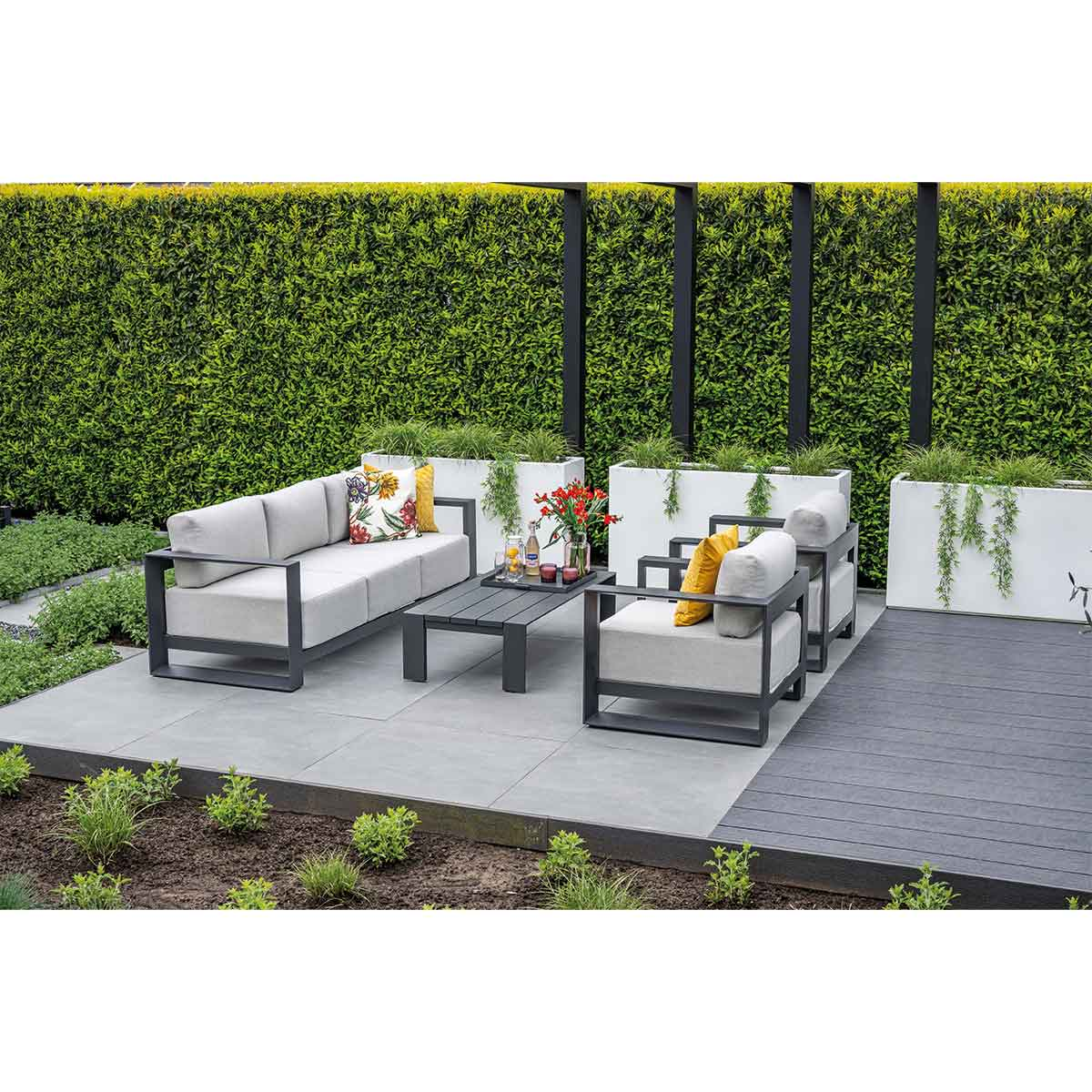 Modern outdoor seating set on patio with green hedge background.