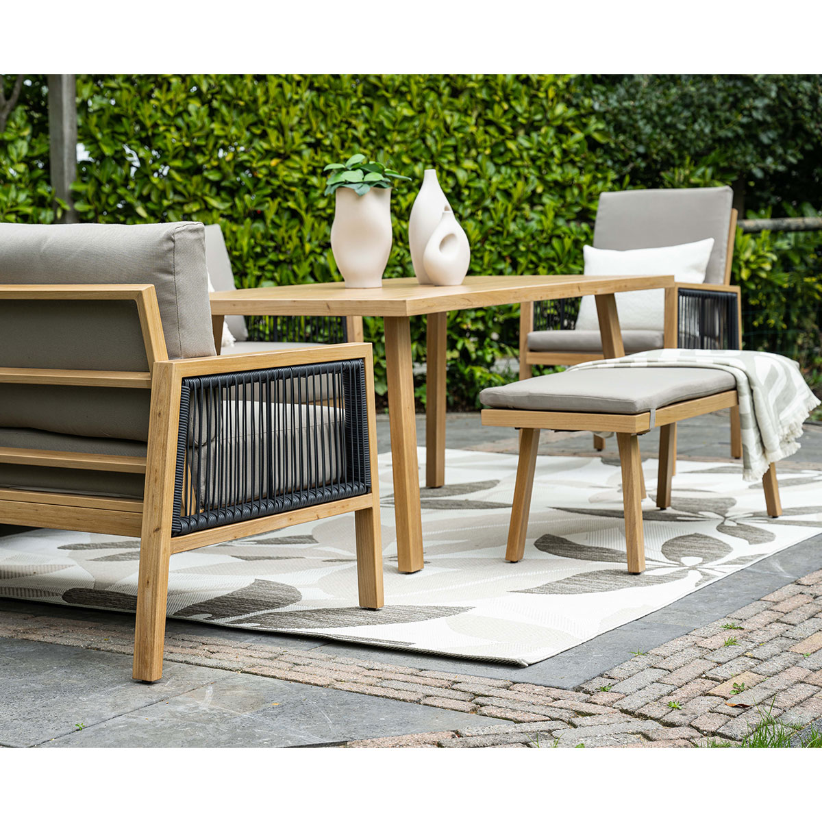 Outdoor setting: sofa, two armchairs, bench, and a table with decor, on a stone patio.