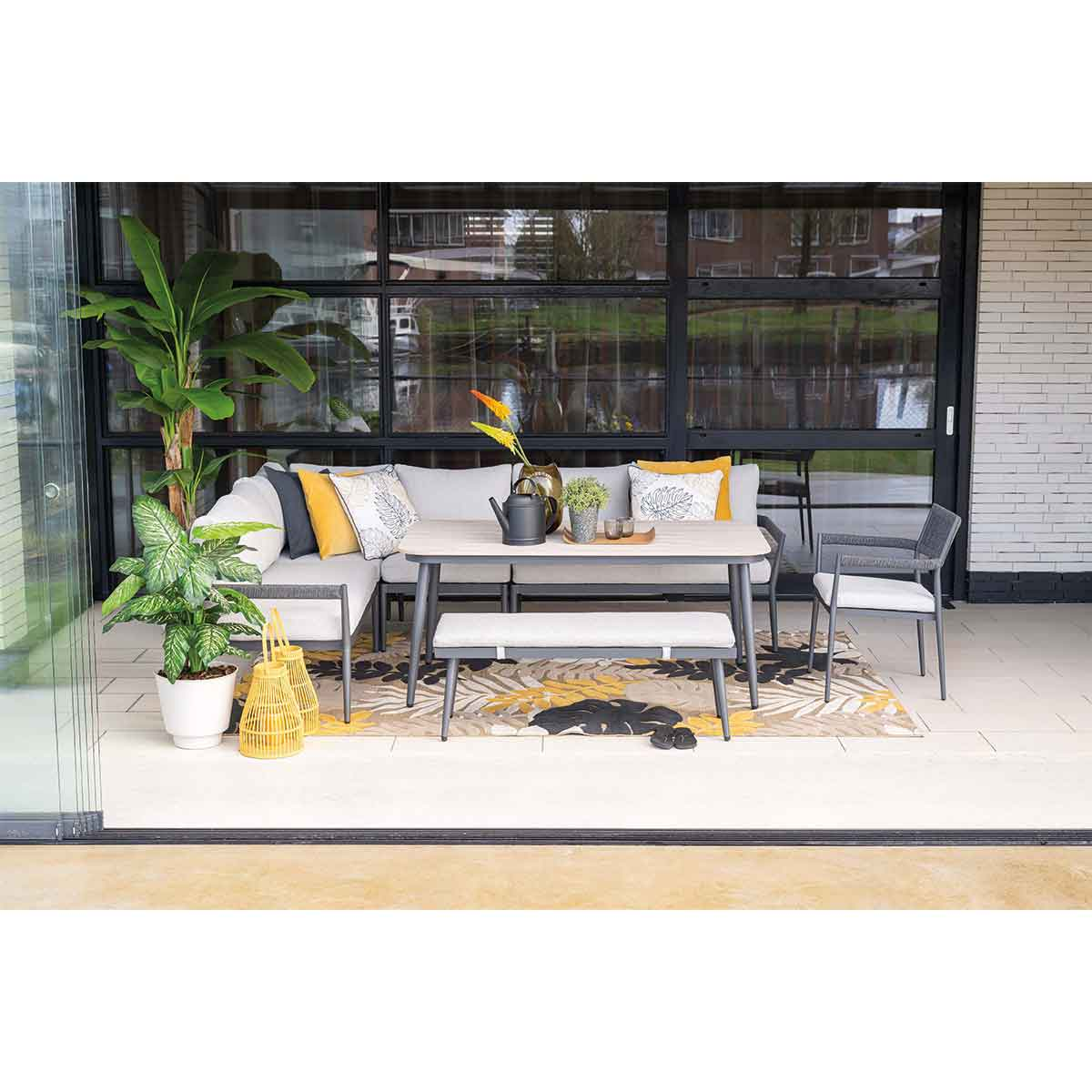 Outdoor patio set with sofa, table, and chairs. Dark metal frames, neutral cushions, and plants.