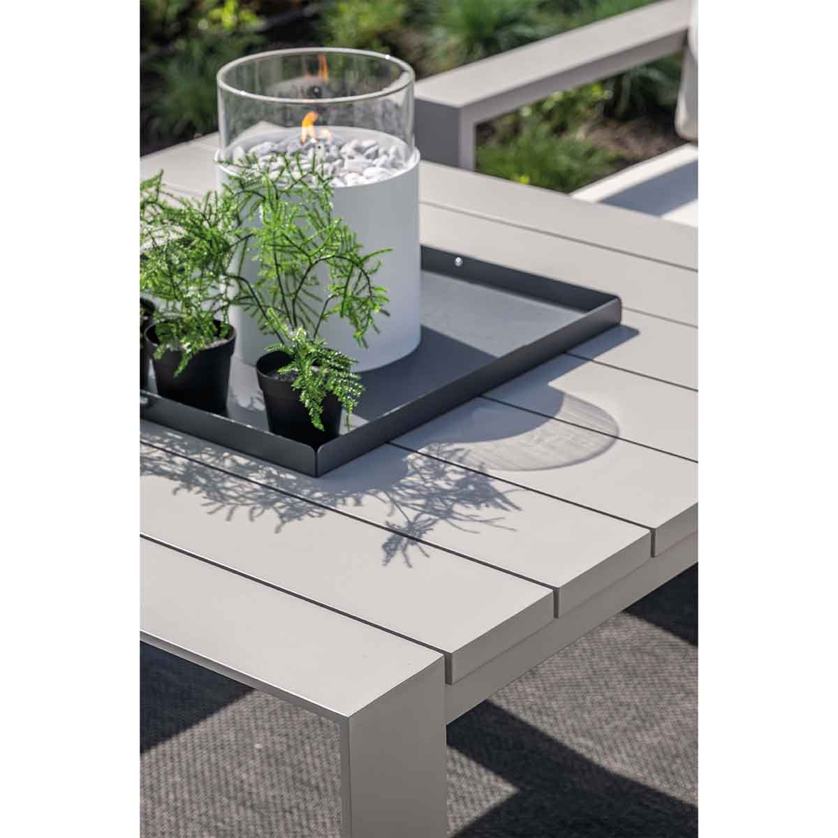 Close-up van een tafel met planten, een glazen lantaarn en een dienblad op een grijs oppervlak.