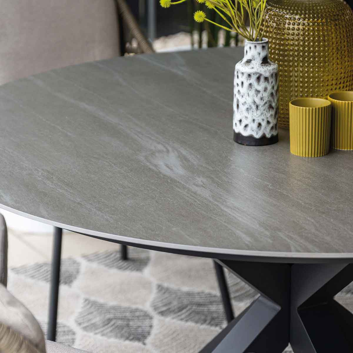 Table ronde grise avec décor, tapis à motifs et base en métal noir.