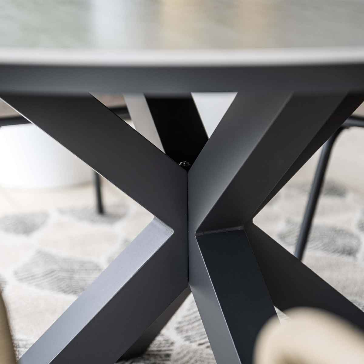 Gros plan d'un pied de table noir avec un design en forme de X et un tapis beige clair en dessous.