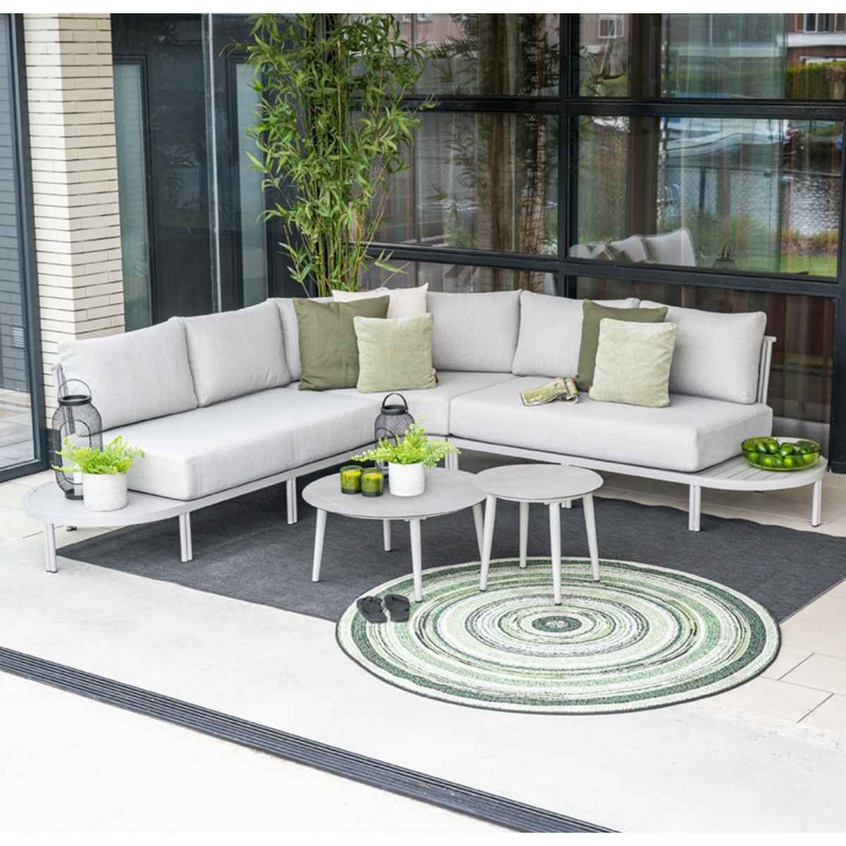 Outdoor seating area with a grey sectional sofa, tables, and a patterned rug.