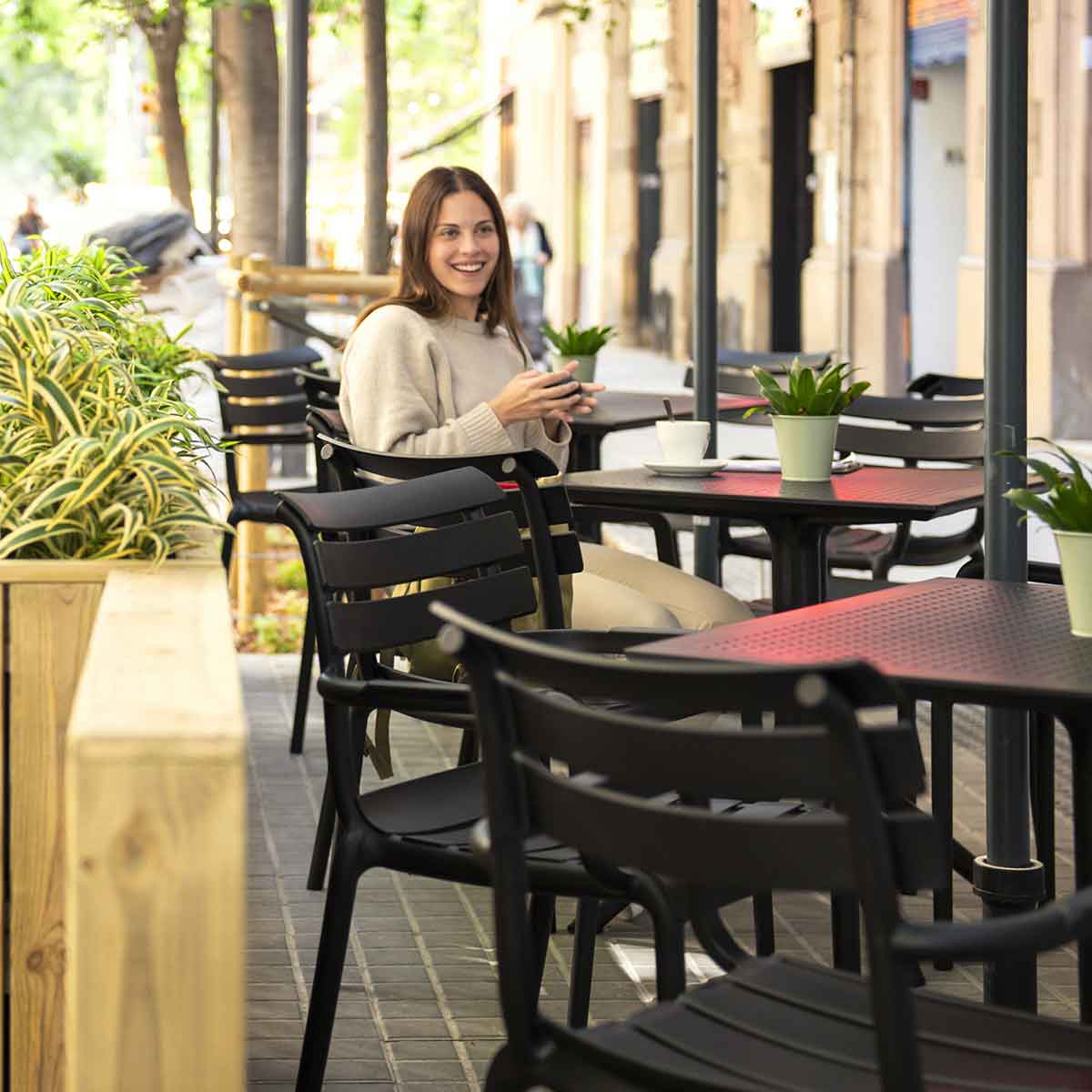 Vrouw zit aan tafel, met stoelen en planten eromheen.