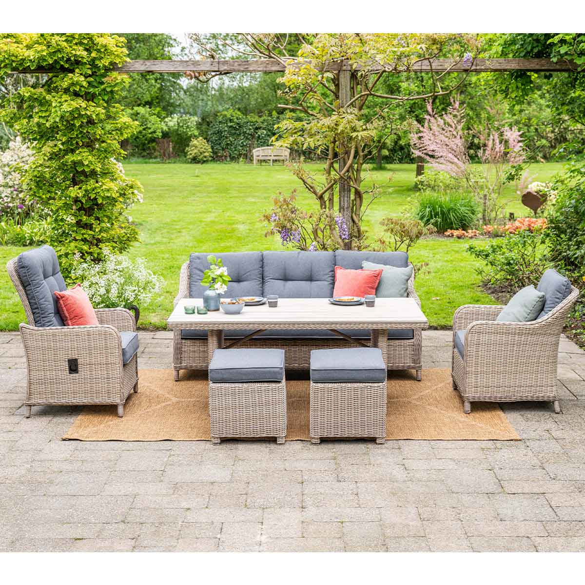 Outdoor patio set. Rattan sofa, armchairs, ottomans, table. Cushions, plants and garden.