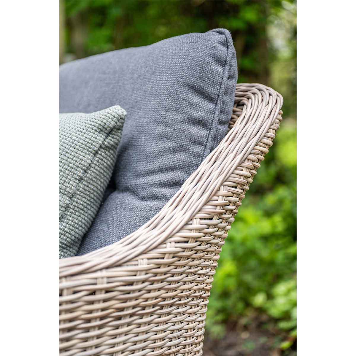 Close-up of rattan armchair. Grey cushion and green pillow.