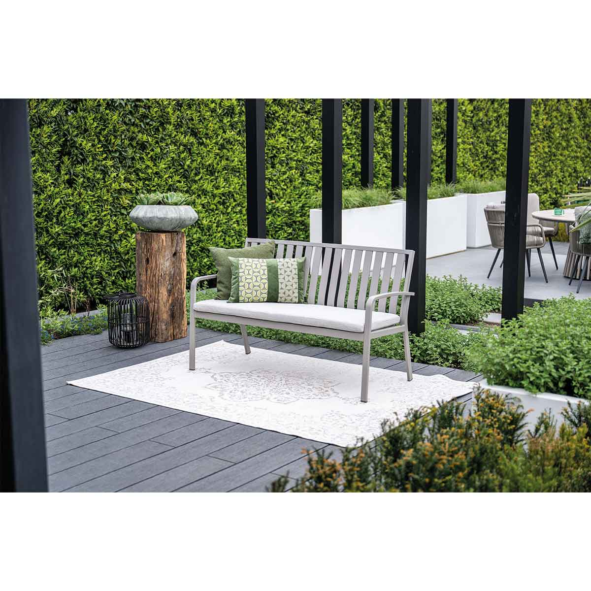 Banc extérieur avec coussins sur un patio. Fond de jardin.