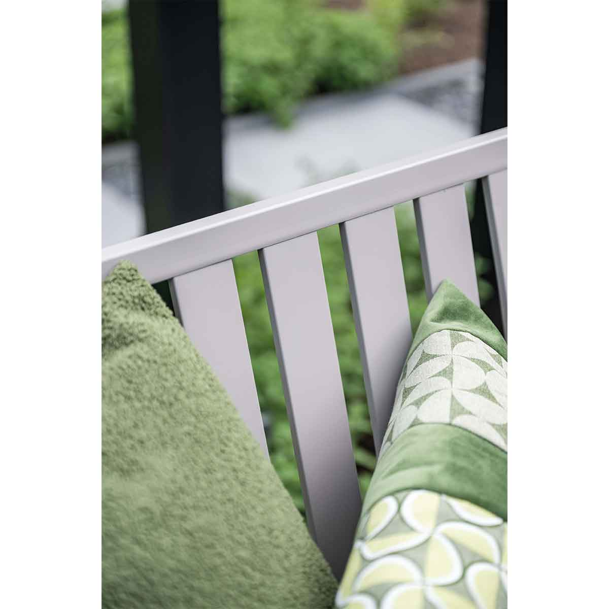 Gros plan sur un oreiller vert avec un motif blanc et un oreiller vert flou sur un banc gris à lattes verticales.