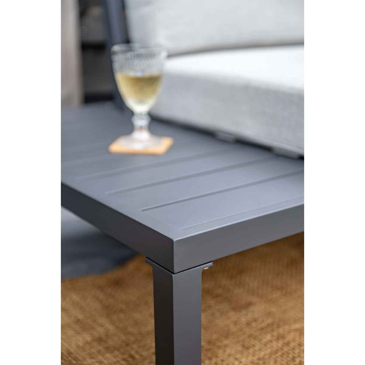 Close up of a table with a drink and a coaster on it, near a sofa with white cushions.