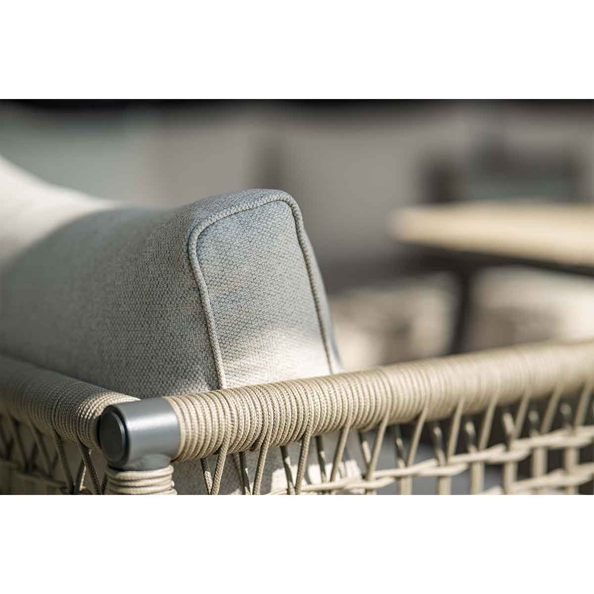 Gros plan d'un coussin gris sur un canapé. Le canapé a un design en rotin tressé.