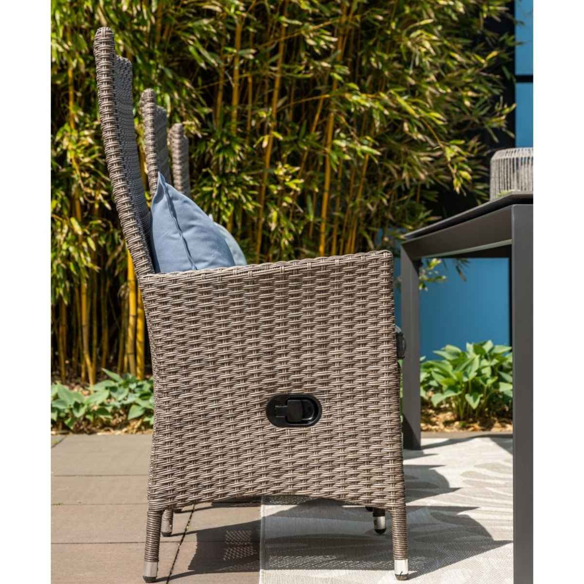Profile view of a wicker chair with cushion, in a garden.