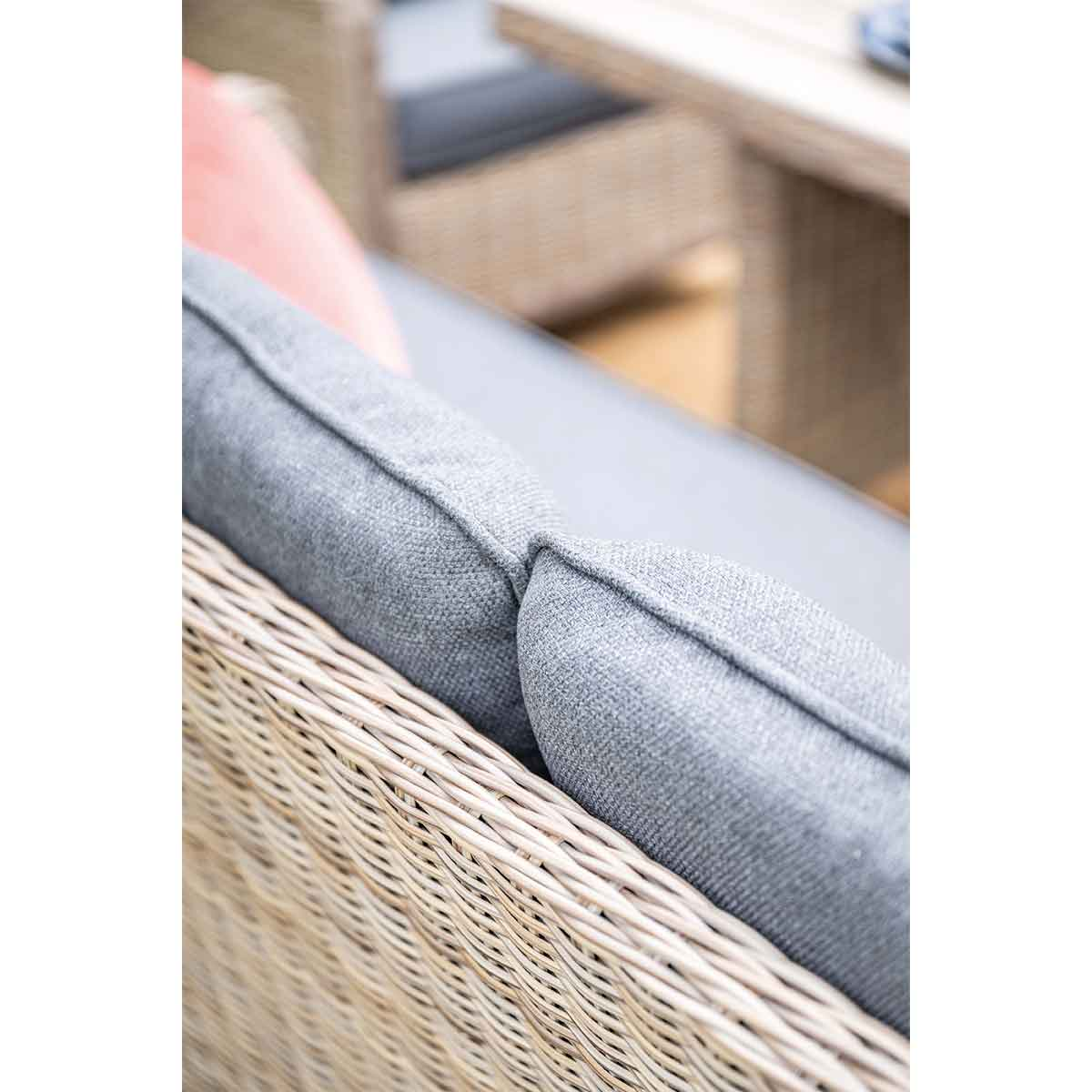 Close-up of a gray cushion on a wicker chair, with a pink pillow visible in the background.
