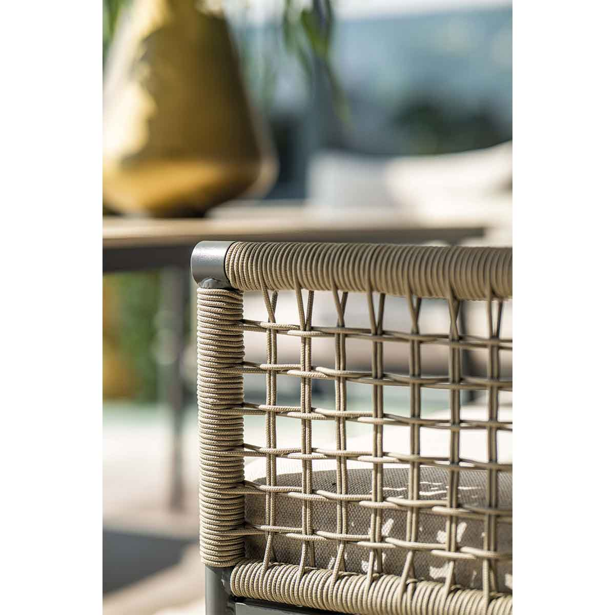Gros plan sur le dossier tissé d'une chaise avec un coussin gris, une table et un vase en arrière-plan.