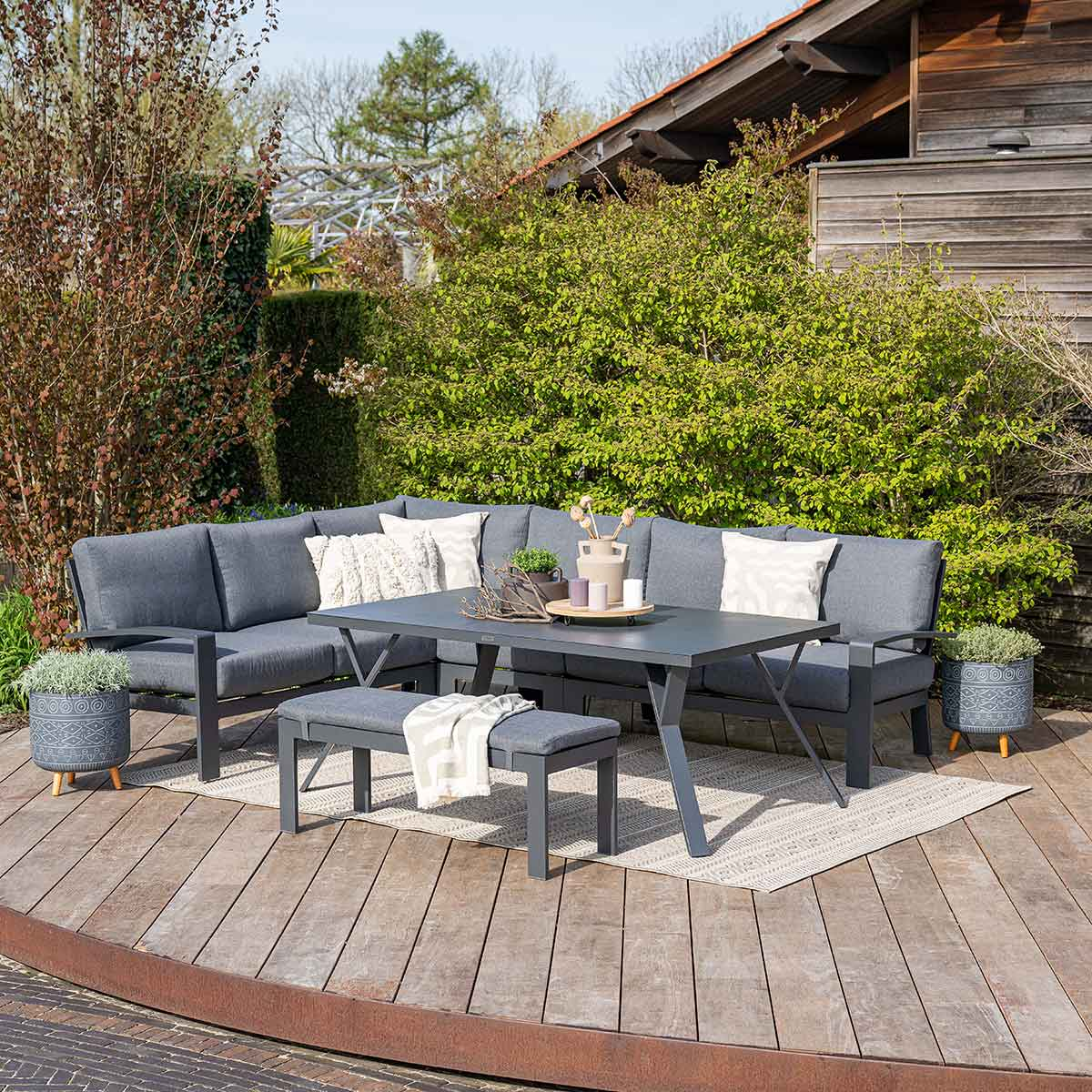Buitenzitgroep met een tafel, bank en grijze kussens, in een tuinsetting.