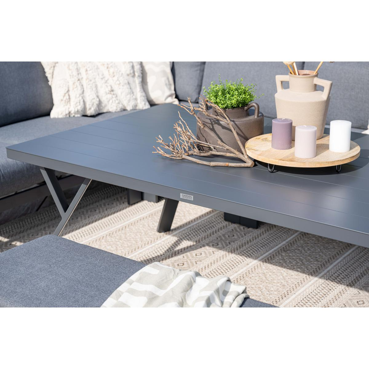 Een grijze buitentafel met decoratieve items en een bank op een kleed.