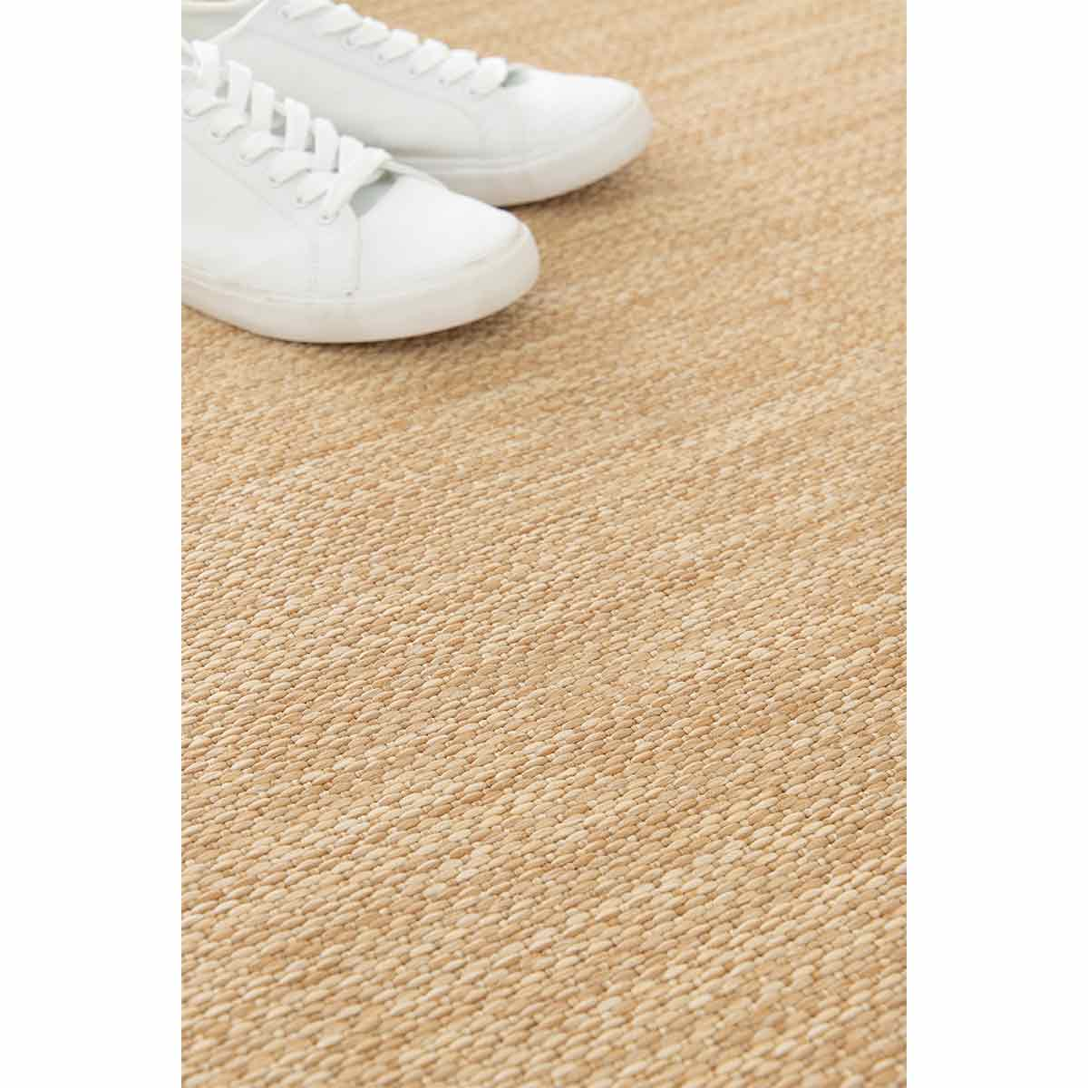 Paar witte sneakers op een beige vloerkleed. Close-up.