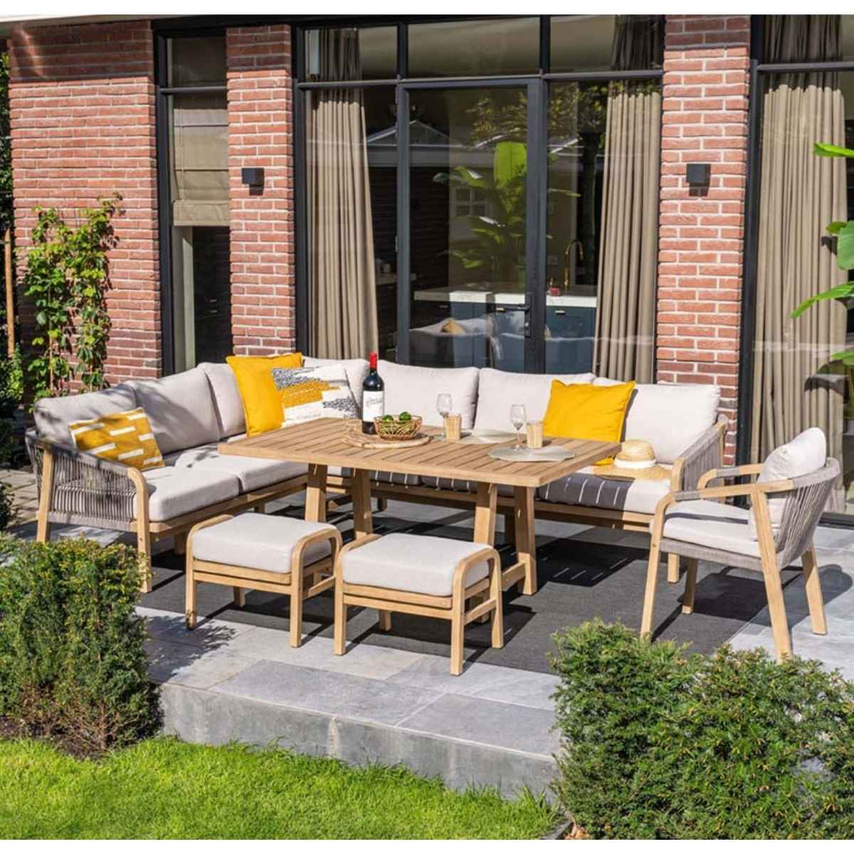 Outdoor seating arrangement with a table, sofa, chairs, and ottomans.  Neutral colors, brick background.