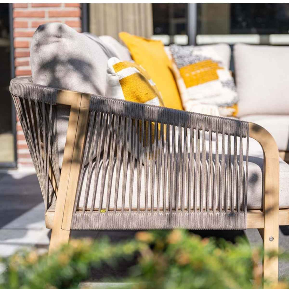 Outdoor sofa with gray cushions and wooden frame, with yellow and white pillows.