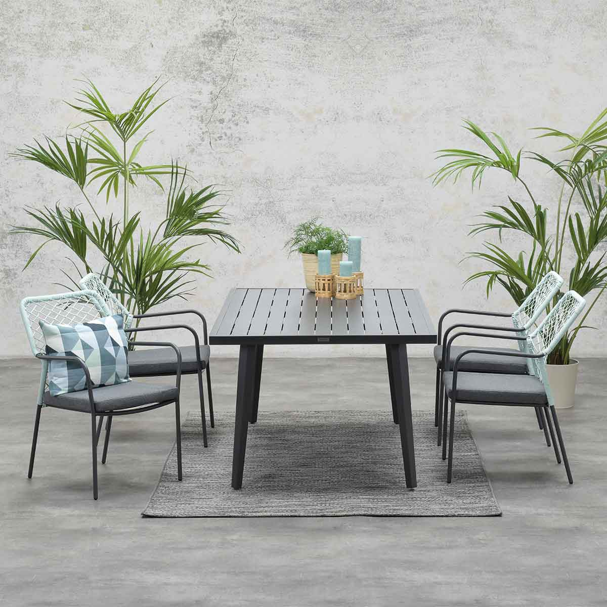 Outdoor dining set with table and chairs. Plants in background. Gray floor.