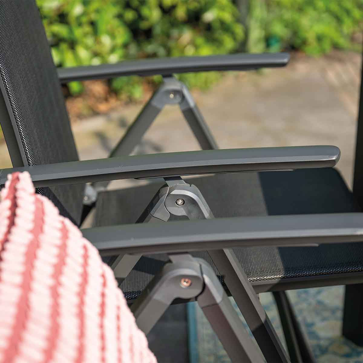 Close up of a grey folding chair. Grey frame and black mesh seat. Pink striped pillow.
