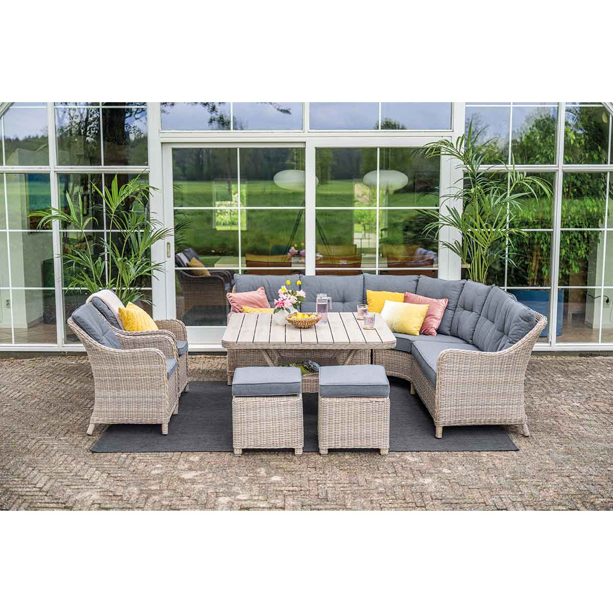 Outdoor furniture set. L-shaped sofa with cushions, two ottomans, table, and chairs. House in background.